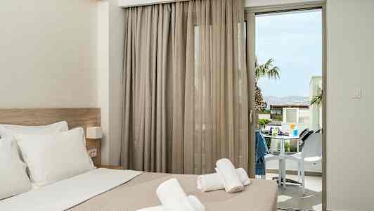 Hotelværelse med redt seng og håndklæder placeret ovenpå, med en altandør der vender ud mod en terrasse. (AI-genereret tekst)