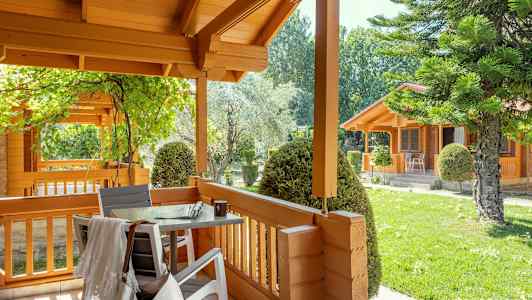 En træveranda med bord og stole, omgivet af grønne områder og træhuse. (AI-genereret tekst)