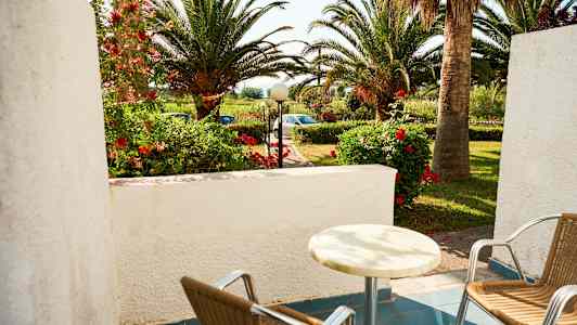 En terrasse med to stole og et bord, have med palmer og blomster i baggrunden. (AI-genereret tekst)