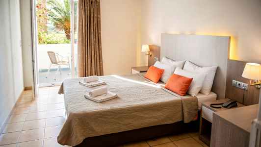 Billede af et hotelværelse med dobbeltseng, to røde puder og et vindue, der fører til en balkon. (AI-genereret tekst)