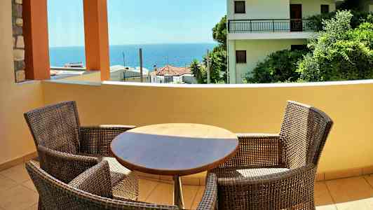 Altan med bord og stole samt udsigt over hav og bygninger. (AI-genereret tekst)