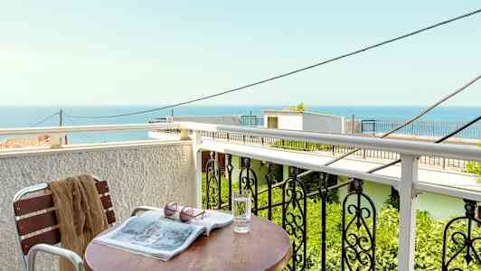 En altan med udsigt over havet, et bord med et glas vand, en avis og solbriller. (AI-genereret tekst)