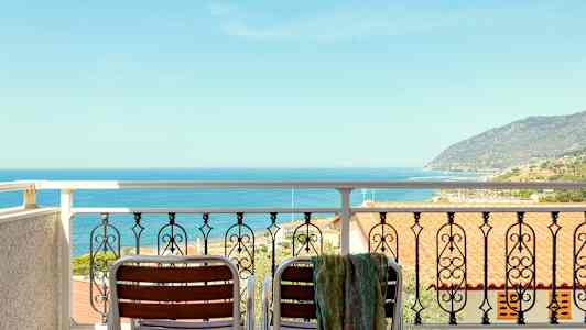 Udsigt fra en balkon med to stole og et rækværk mod havet og en kystlinje. (AI-genereret tekst)