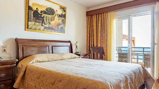 Et hotelværelse med en stor seng, trædetaljer og en balkon med havudsigt. (AI-genereret tekst)