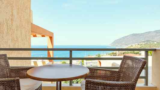 Udsigt over havet fra en balkon, med to flettede stole og et bord i forgrunden. (AI-genereret tekst)