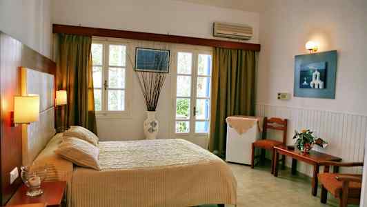 Hotelværelse med seng, bord og stole, vindue med gardiner. (AI-genereret tekst)