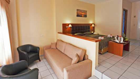 Et hotelværelse med en sofa, to lænestole og en seng bag en lav skillevæg. (AI-genereret tekst)