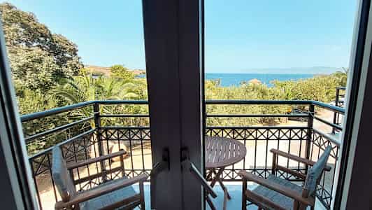 Udsigt fra en altan med to stole og et bord, havet og træer ses i baggrunden. (AI-genereret tekst)