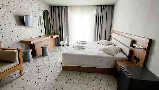 Et hotelværelse med seng, skrivebord og stol, samt lyse gardiner ved vinduet. (AI-genereret tekst)