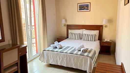 Et hotelværelse med en redt dobbeltseng, vindue med lyse gardiner og trømøbler. (AI-genereret tekst)