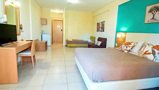 Et hotelværelse med en seng, sofa, skrivebord og tv samt en dør til en anden del af rummet. (AI-genereret tekst)