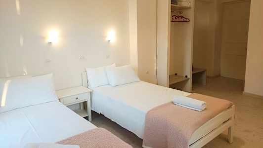 To enkeltsenge med hvide lagner og lyserøde tæpper står i et lyst rum. (AI-genereret tekst)