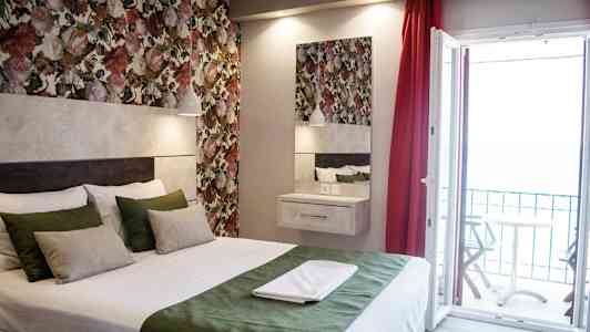 Et værelse med en seng, farverige blomster vægge og en åben altandør. (AI-genereret tekst)