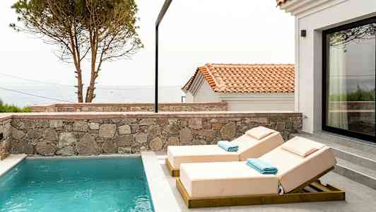 Udendørs pool med to liggestole og udsigt over havet og hustage. (AI-genereret tekst)