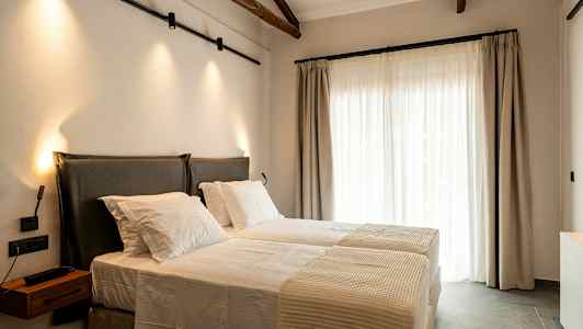 Et soveværelse med to senge, oplyst af væglamper, med store vinduer dækket med lyse gardiner. (AI-genereret tekst)