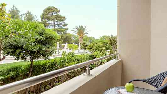 En altan med udsigt over træer og en pool, med et bord og en stol i forgrunden. (AI-genereret tekst)