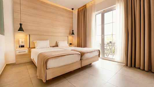 To enkeltsenge i et lyst rum med store glasdøre og beige gardiner. (AI-genereret tekst)