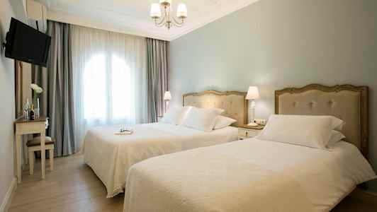 Hotelværelse med to enkeltsenge, lys indretning og vindue med gardiner. (AI-genereret tekst)