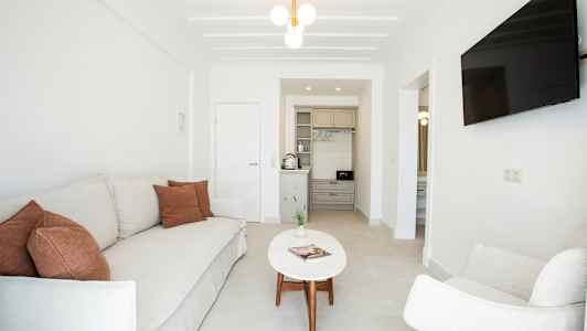 Stue med sofa, lænestol, sofabord, TV og et lille køkken. (AI-genereret tekst)