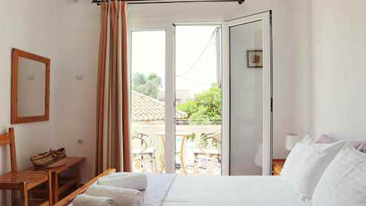 Et lyst soveværelse med hvide vægge, en seng med hvidt sengetøj og en balkon udenfor glasdøre. (AI-genereret tekst)