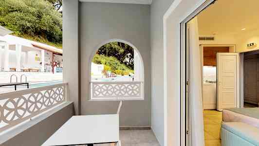 En altan med et hvidt bord og en stol, udsigt til poolområdet og kig ind i et værelse. (AI-genereret tekst)