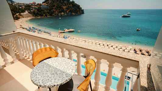 Udsigt fra en balkon mod en sandstrand med parasoller og klart blåt hav. (AI-genereret tekst)