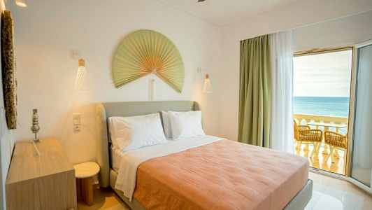 Soveværelse med en dobbeltseng, dekoreret med en stor vifte på væggen og en altan med udsigt over havet. (AI-genereret tekst)