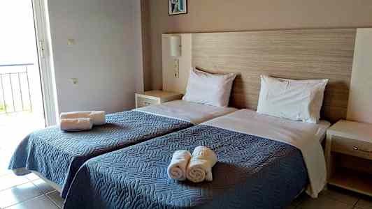 Rummet har to enkeltsenge med blåt sengetæpper og hvide puder samt rullede håndklæder placeret på sengen. (AI-genereret tekst)