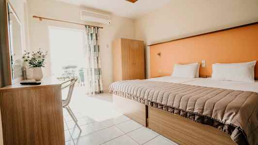 Et lyst hotelværelse med en redt seng, skrivebord og stol samt et klædeskab. (AI-genereret tekst)