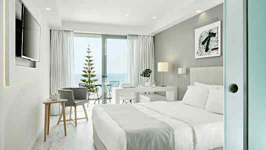 Moderne hotelværelse med dobbeltseng, skrivebord og skydedør ud til en balkon med havudsigt. (AI-genereret tekst)