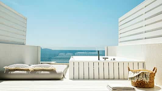 En hvid terrasse med et spabad, puder og udsigt over havet. (AI-genereret tekst)