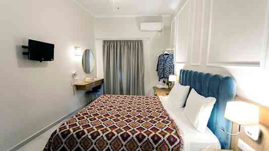 Et hotelværelse med en seng, vægmonteret tv, skrivebord og et gardin ved vinduet. (AI-genereret tekst)