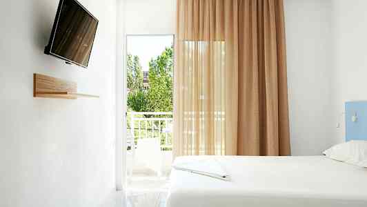 Et lyst værelse med en seng, en vægmonteret TV og en balkon med udsigt. (AI-genereret tekst)