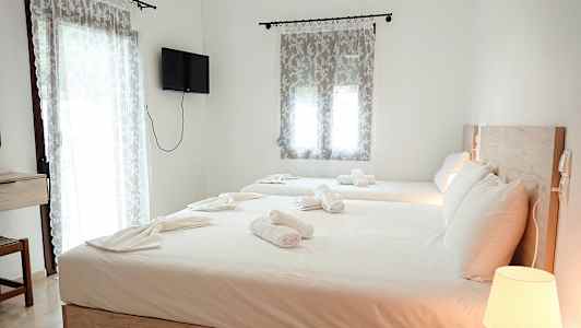 Et hotelværelse med to senge, redt med hvide sengelagner og håndklæder. En lampe på et natbord og et vægmonteret TV ses i rummet. (AI-genereret tekst)