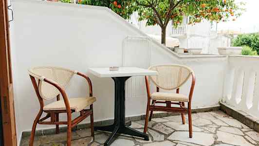 En lille terrasse med to stole og et bord foran et appelsintræ. (AI-genereret tekst)