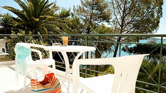 Udendørsmøbler på en balkon med udsigt til træer og vand. (AI-genereret tekst)