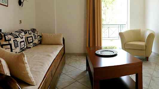 Et opholdsrum med en sofa med geometriske mønstre, et rundt bord og en lys lænestol ved et vindue. (AI-genereret tekst)