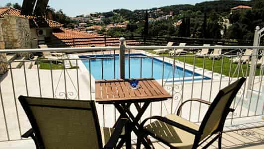 Udsigt fra en terrasse mod en pool og et landskab med huse og grønne områder. (AI-genereret tekst)