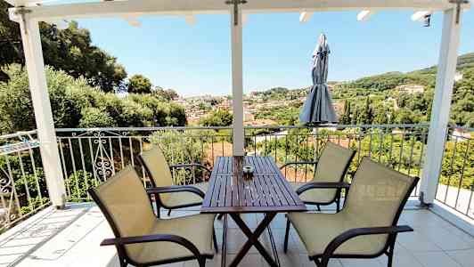 Udendørsområde med bord og stole, udsigt over grønt landskab og bygninger. (AI-genereret tekst)