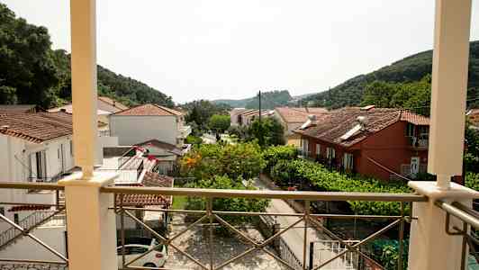 Udsigt fra en altan over huse med tegltage og grønt samt bjerge i baggrunden. (AI-genereret tekst)