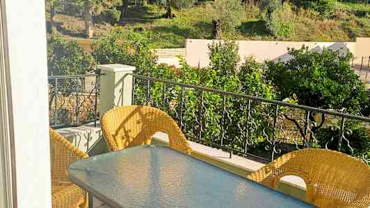 Altan med bord og stole i sollys, omgivet af grønne områder og træer. (AI-genereret tekst)