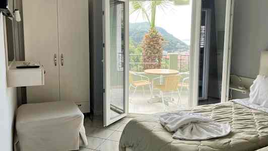 Hotelværelse med udsigt til en terrasse med bord, stole og en palme. (AI-genereret tekst)