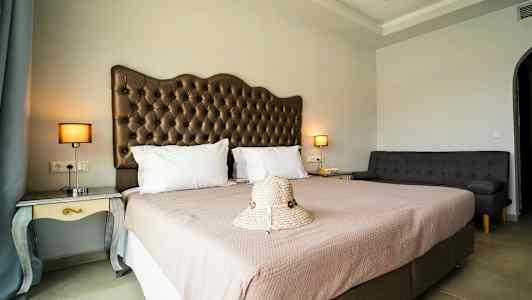 Et hotelværelse med en dobbeltseng, en sofa og natborde med lamper, samt en hat placeret på sengen. (AI-genereret tekst)