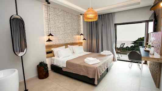 Et moderne hotelværelse med en stor seng, lyse vægge og en dør, der åbner ud til en altan med havudsigt. (AI-genereret tekst)