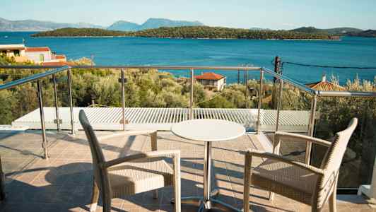 To stole og et lille bord på en terrasse med glasrækværk, udsigt til havet og skovklædte øer. (AI-genereret tekst)