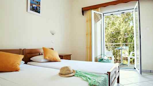 Et hotelværelse med enkeltsenge, åbent vindue og udsigt til balkon. (AI-genereret tekst)