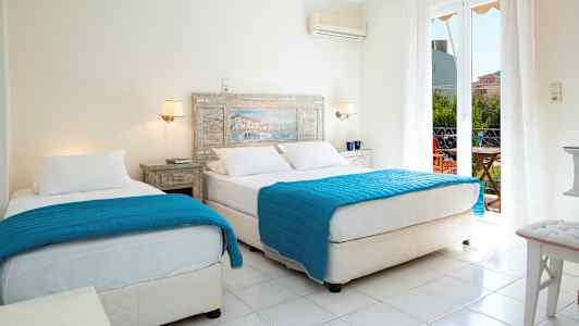 Et hotelværelse med to senge med blå tæpper og hvide lagner. En glasdør fører til en balkon. (AI-genereret tekst)