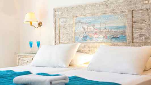 Dobbeltseng med hvide puder, blåt sengetæppe og en væglampe. (AI-genereret tekst)