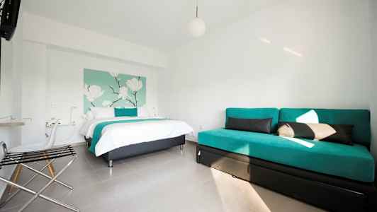 Et hotelværelse med en seng og en sofa, indrettet i lyse farver. (AI-genereret tekst)