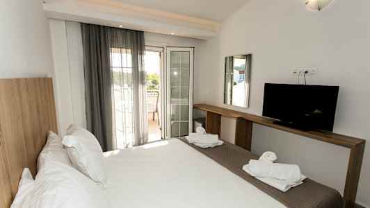 Et hotelværelse med en dobbeltseng, en TV på en træbænk og en altan med udsigt. (AI-genereret tekst)